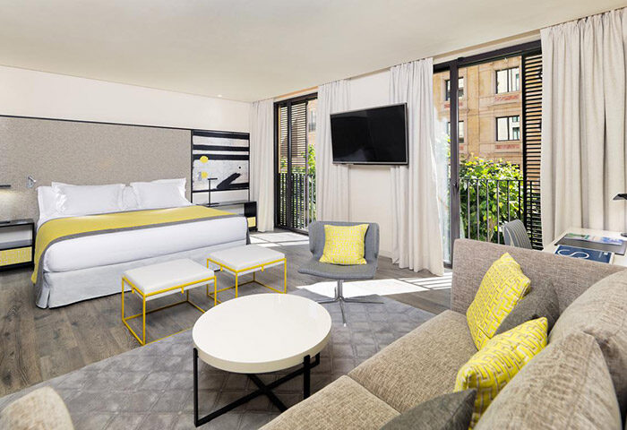 H10 Art Gallery Hotel stylish room design. Gay hotel in Barcelona's Gaixample district. Modern decor with bed, sofa, & balcony.