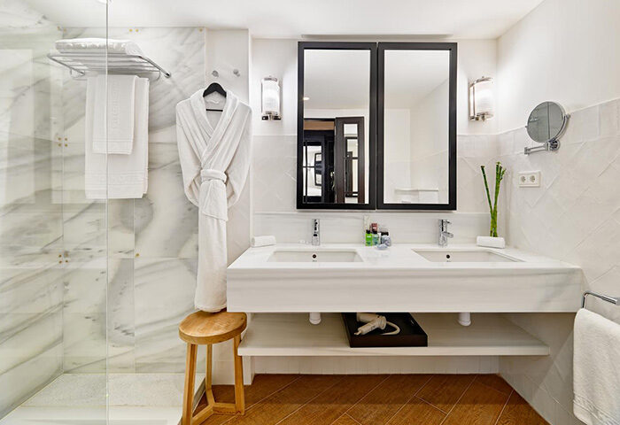 H10 Metropolitan Hotel bathroom. Most booked gay hotel in Barcelona's tourist area. Double sink, robe, stool, and shower.