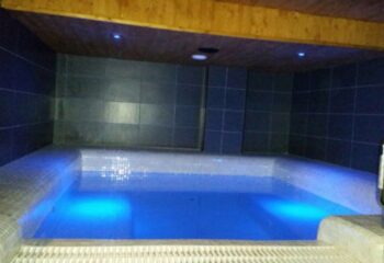 H2O Sauna, Benidorm. Interior view of the gay sauna's pool with blue lighting, tiled walls, and wooden ceiling, a relaxing space.