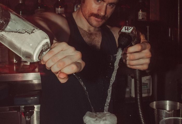 Bartender at HUSH HK, a gay bar and dance club in New York, pouring drinks. Nightlife scene for gay men traveling to NYC.