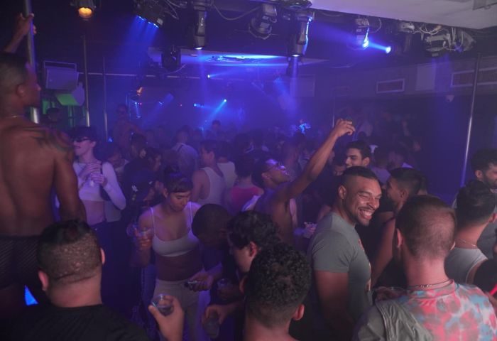 HUSH HK Gay Bar Dance Club in New York. Crowd of gay men dancing, shirtless dancer on pole, blue lights, nightlife scene, travel advice.