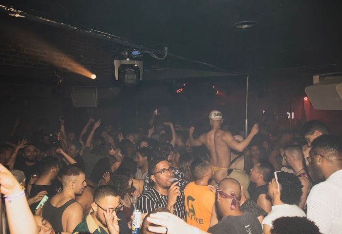 HUSH HK gay bar, dance club in New York. Crowd of gay men dancing, shirtless dancer on stage. Nightlife, travel advice, gay scene.