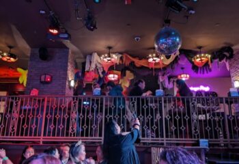 Hamburger Mary's Long Beach experience. Crowded gay bar with disco ball, stage, and patrons enjoying a night out. Fun, lively atmosphere.