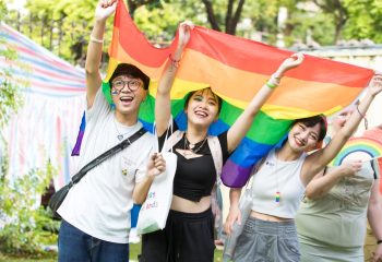Hanoi Pride: Smiling people holding a rainbow flag. Gay travel in Vietnam. LGBTQ+ community celebrates diversity and equality.