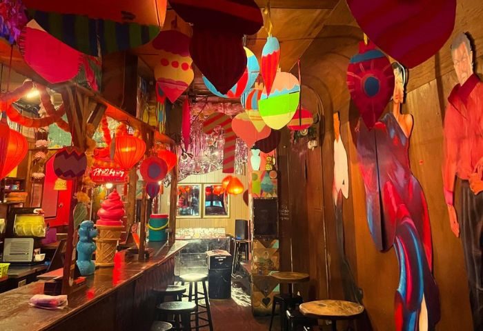 Interior of Happyfun Hideaway, a gay bar in New York. Colorful decorations, bar stools, and unique artwork create a fun, vibrant atmosphere.