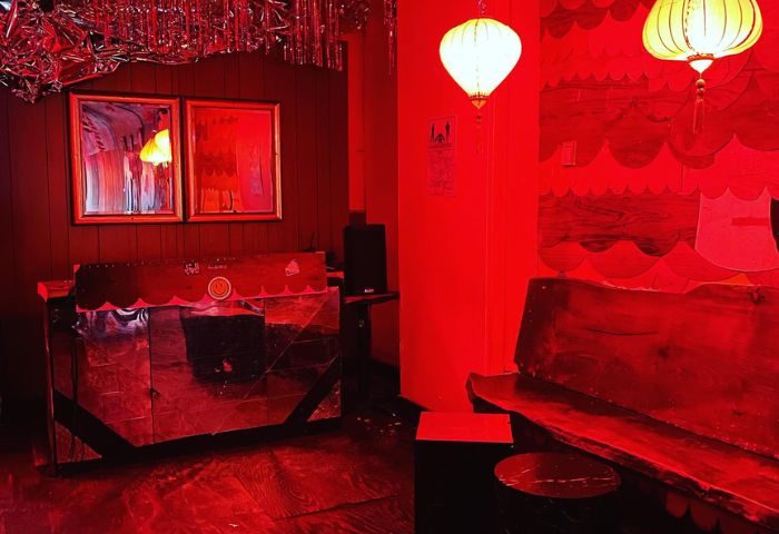Interior of Happyfun Hideaway, a gay bar in New York, lit in red. Lanterns hang above a wooden bench and mirrored bar. Quirky, fun decor.