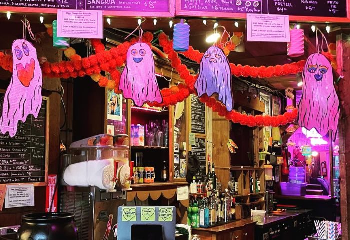 Happyfun Hideaway gay bar in New York, decorated for Halloween. Ghosts hang above the bar, which is stocked with drinks and a slushy machine.