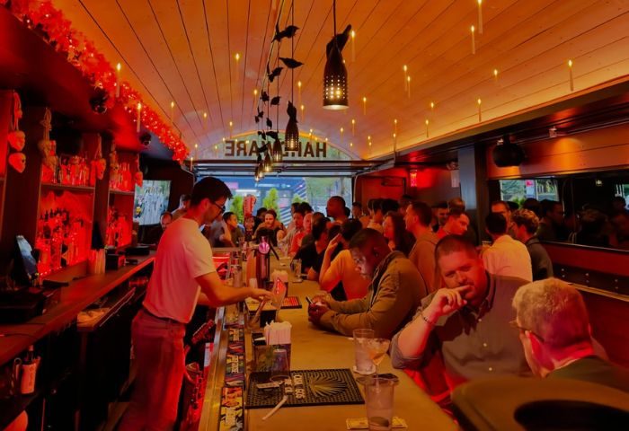 Hardware Bar in New York. A busy gay bar scene with a bartender serving drinks and patrons enjoying themselves in a warm, inviting space.