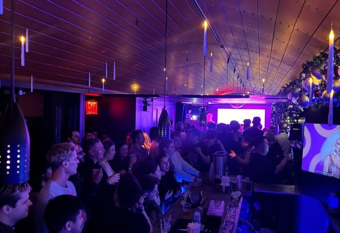 Crowded Hardware Bar in New York. Gay men gather, enjoying drag show entertainment. Festive decor, vibrant nightlife scene.