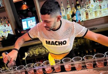 Bartender at Hardware Bar in New York. Man in MACHO shirt pours drinks. Gay nightlife, travel advice, bar scene. Cocktails.