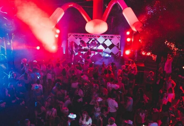 Heaps Gay Sydney event with a crowd of people dancing under red & blue lights. DJs are on stage. Gay travel advice.