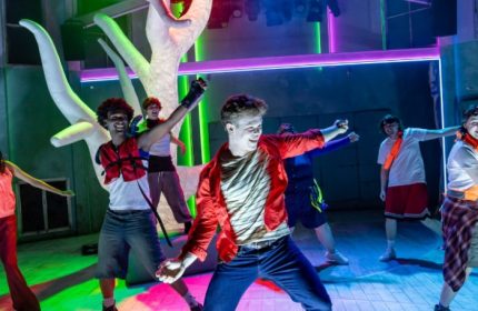 Heaps Gay Sydney performance art scene. Energetic group of young people dancing on stage with vibrant lighting. Gay travel guide.