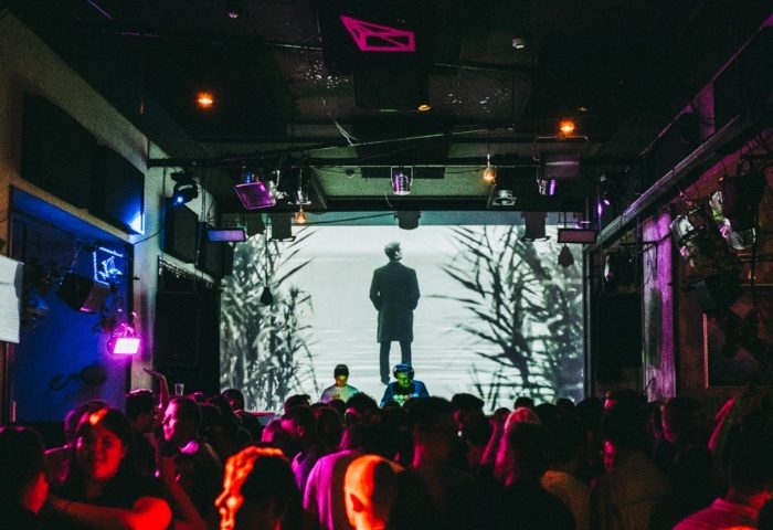 Gay party at Toldi Club in Budapest. Crowd of people dancing, DJs performing, and a large screen displaying visuals. Gay travel.