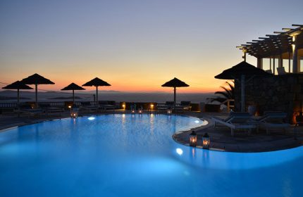 Rooftop pool view at sunset, Hermes Mykonos Hotel, a popular gay hotel. Umbrellas, lounge chairs, and lanterns surround the pool.