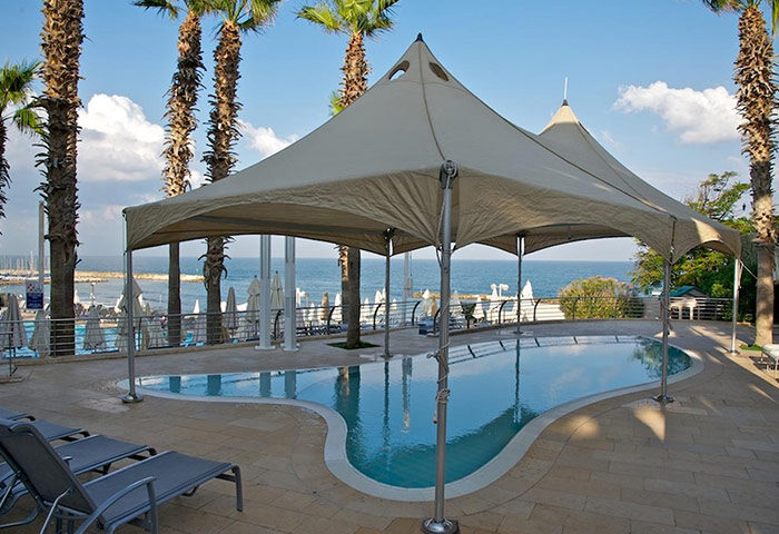 Hilton Tel Aviv beachfront luxury gay hotel pool. Palm trees, sunshades, and lounge chairs create a relaxing gay travel vibe.