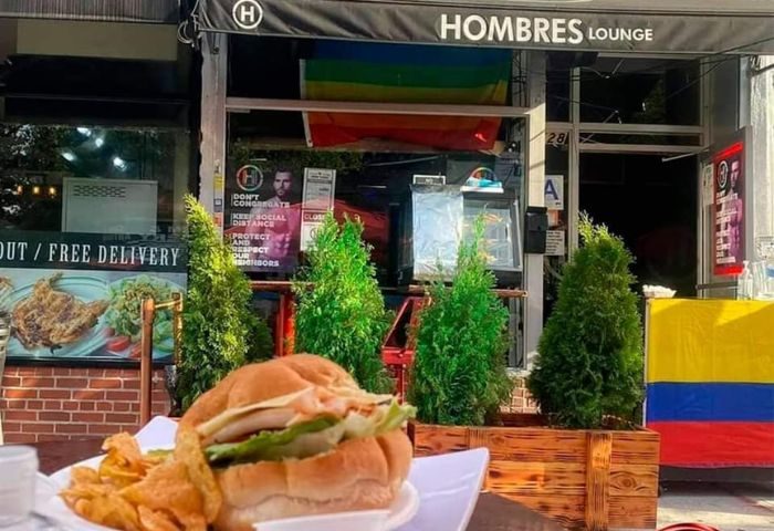 Hombre's Lounge in New York: Gay bar's outdoor seating with burger and chips. Rainbow flag visible. Gay travel advice for LGBTQ+ visitors.