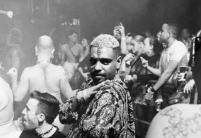 Homoelectric Manchester: Gay men dancing at a club. Black and white photo of a crowded dance floor, featuring a man in patterned shirt.