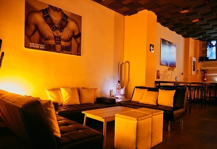 Interior of Honey, a furry gay bar in Barcelona. Couches, tables, and a suggestive art piece create a welcoming space.