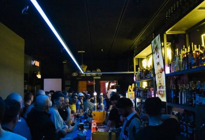 Interior of Honey, a furry gay bar in Barcelona. Men are standing at the bar, with liquor bottles on shelves behind.