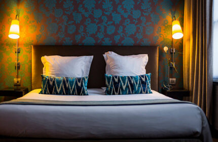 Duo Hotel room, a honeymoon hotel idea for gay couples in Paris. Bed with patterned pillows and wallpaper. Gayborhood hotel in Paris.