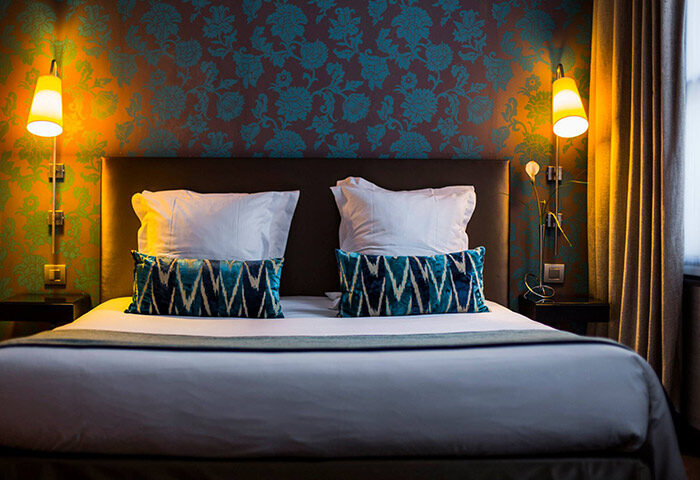 Duo Hotel room, a honeymoon hotel idea for gay couples in Paris. Bed with patterned pillows and wallpaper. Gayborhood hotel in Paris.