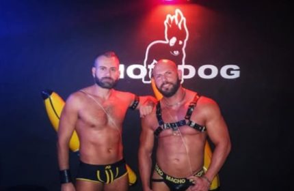 Two muscular men pose at Hot Dog Club Milan. One wears a harness, the other briefs. Gay travel hotspot. Nightlife.