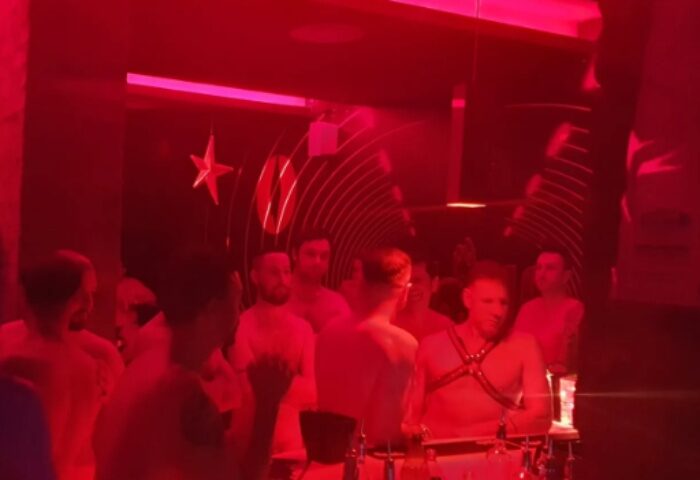 Hot Dog Club Milan: Gay men in red-lit club. Some are shirtless, one in harness. Star decoration on wall. Gay travel advice.
