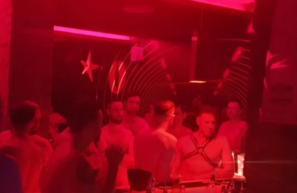 Hot Dog Club Milan: Gay men in red-lit club. Some are shirtless, one in harness. Star decoration on wall. Gay travel advice.
