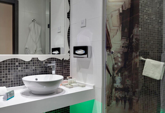 Hotel Indigo Madrid Gran Via bathroom. Modern design with a round sink, decorative mirror, and shower with a Gran Via street scene.
