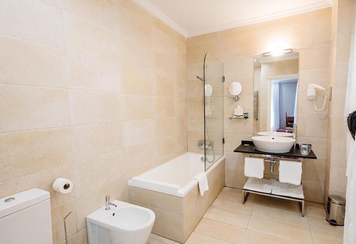 Hotel Infantas by MIJ bathroom. Best boutique gay hotel in Chueca, Madrid gayborhood. Bathtub, bidet, sink, mirror, and beige tile.