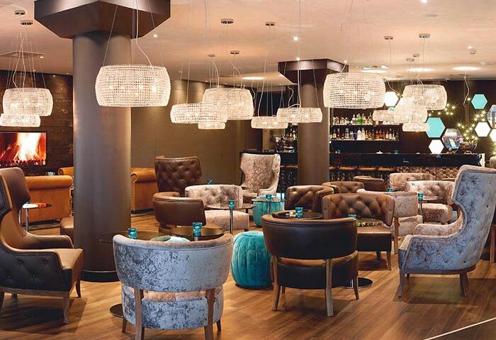 Hotel Motel One London Tower Hill lounge area. Stylish chairs, bar, and lighting. Gay travel advice for a chic, relaxed atmosphere.