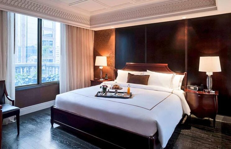 Hotel Muse Bangkok room: luxurious king bed with breakfast tray, dark wood accents, city view. Gay travel destination.