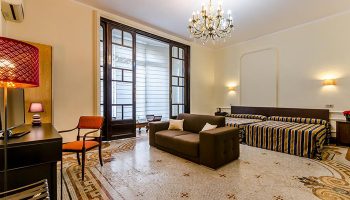 Hotel Victoria Palace Barcelona room. Most booked gay hotel near Sauna BRUC. Suite with sofa, beds, chandelier, and mosaic floor.