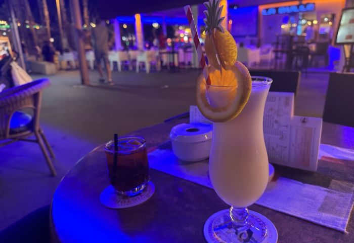 Cocktails at Hummel Hummel Gay Bar, Gran Canaria. A tropical drink with pineapple and orange garnish, plus a dark cocktail on a table.