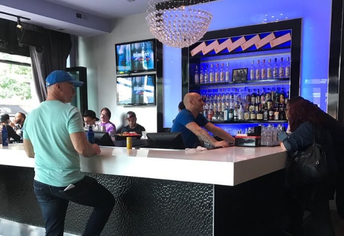 Inside Hydrate Nightclub, Chicago. Bartender serves patrons. TVs, chandelier, & liquor bottles. Gay bar scene, nightlife.