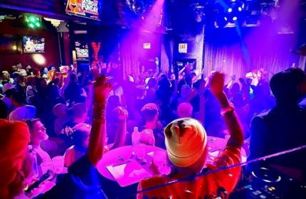 Hydrate Nightclub: Chicago gay bar with a drag show. Crowded dance floor under blue & purple lights. DJ plays music. Gay travel nightlife.