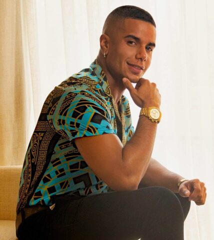 Stylish gay traveler posing with patterned shirt and gold watch. Gay travel advice for men, fashion inspiration.
