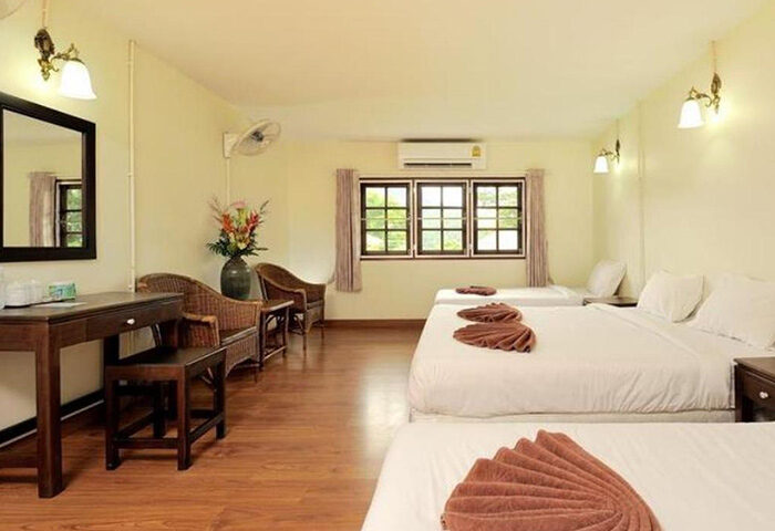 Phi Phi hotel room with three beds, desk, chairs, and a window. This cheap beachfront hotel is perfect for gay men traveling to Ibiza.