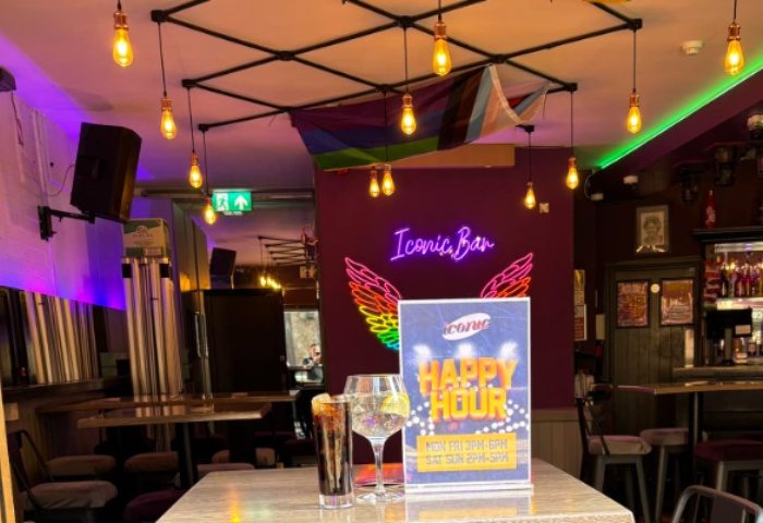 Iconic Bar in Manchester: Interior view with drinks, rainbow flag, neon sign, and happy hour ad. Gay travel advice.