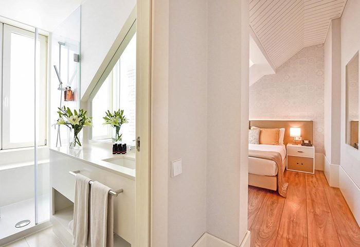 My Story Hotel Ouro room: bathroom with shower, sink, and flowers, leading to bedroom. Ideal honeymoon gay hotel in Lisbon's gayborhood.