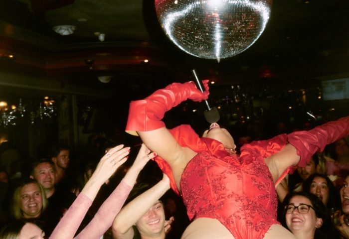 Imperial Erskineville Sydney: Drag queen in red performs under a disco ball, cheered on by a crowd. Gay travel nightlife scene.