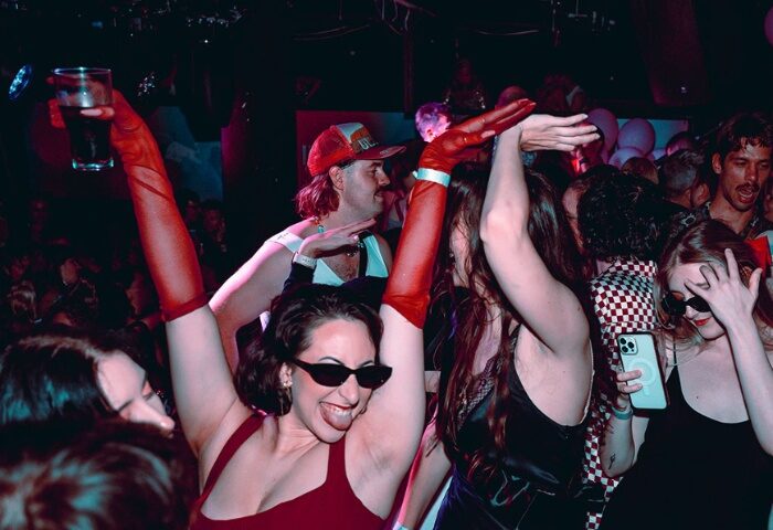Imperial Erskineville Sydney: Partygoers dance at a gay bar, one with red gloves & sunglasses, enjoying Sydney's vibrant nightlife.