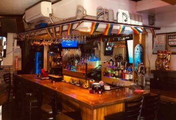 Inside In Between Waikiki gay bar in Honolulu, Hawaii. Rainbow flags, liquor bottles, & karaoke on TV. Gay travel advice.