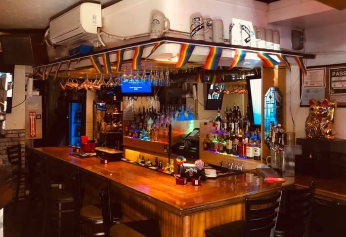 Inside In Between Waikiki gay bar in Honolulu, Hawaii. Rainbow flags, liquor bottles, & karaoke on TV. Gay travel advice.