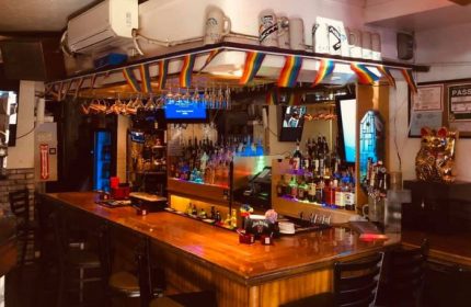 Inside In Between Waikiki gay bar in Honolulu, Hawaii. Rainbow flags, liquor bottles, & karaoke on TV. Gay travel advice.