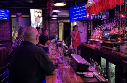 In-Between Waikiki gay bar karaoke in Honolulu. A man sings karaoke at a gay bar in Honolulu, Hawaii, with patrons at the bar.