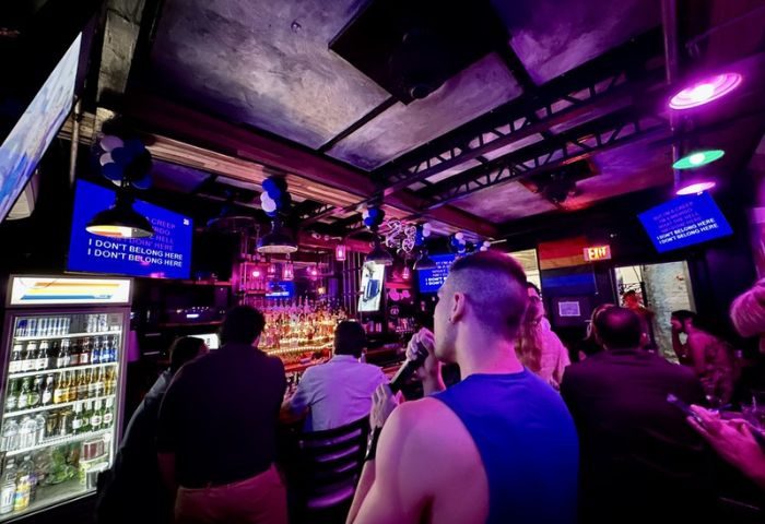 In Between Waikiki gay bar karaoke in Honolulu. A man sings at a bar with a rainbow flag and TV screens with karaoke lyrics.