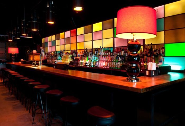 Industry Bar in New York. Long bar with stools, colorful square backlighting, bottles, and lamps. A gay-friendly travel destination.