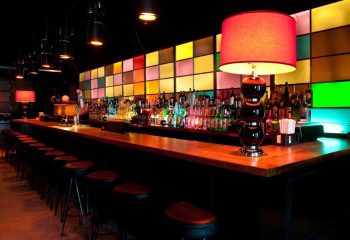 Industry Bar in New York. Long bar with stools, colorful square backlighting, bottles, and lamps. A gay-friendly travel destination.