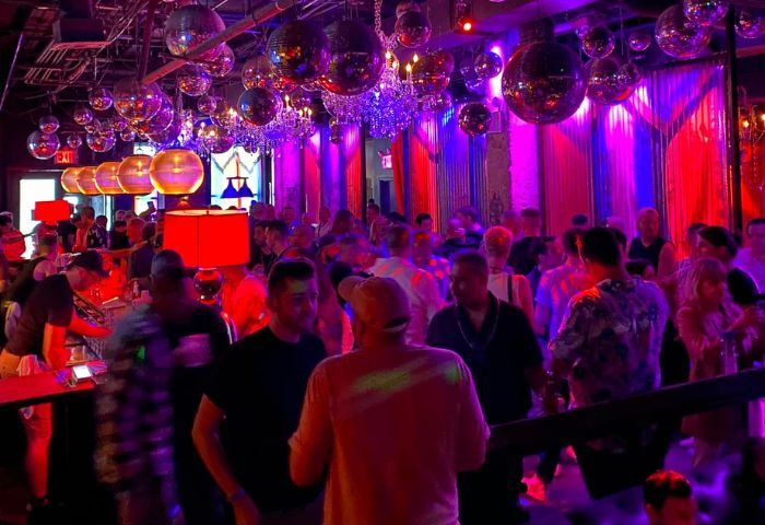 Industry Bar in New York: A lively gay bar scene with a crowd of men under disco balls and colorful lights. Nightlife travel advice.